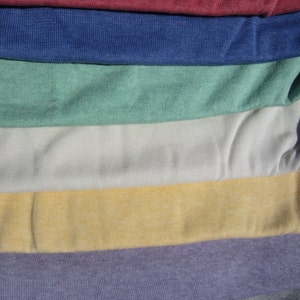 May include: A collection of fabric swatches in various colours, including burgundy, blue, green, white, yellow, purple, and grey. The fabric has a textured, slightly bumpy surface.