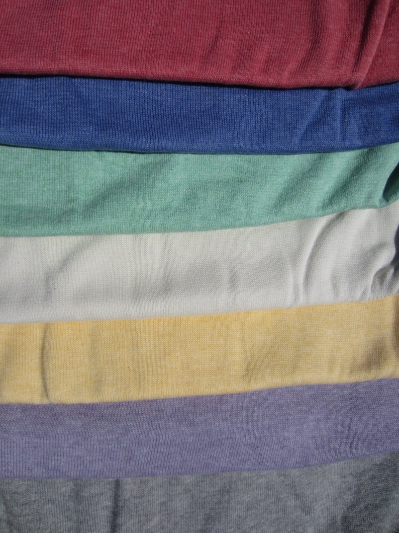 May include: A collection of fabric swatches in various colours, including burgundy, blue, green, white, yellow, purple, and grey. The fabric has a textured, slightly bumpy surface.