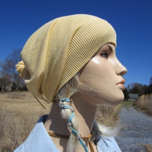 May include: A pale yellow slouchy beanie with a long blue leather cord with silver beads. The beanie is worn by a mannequin with blonde hair.