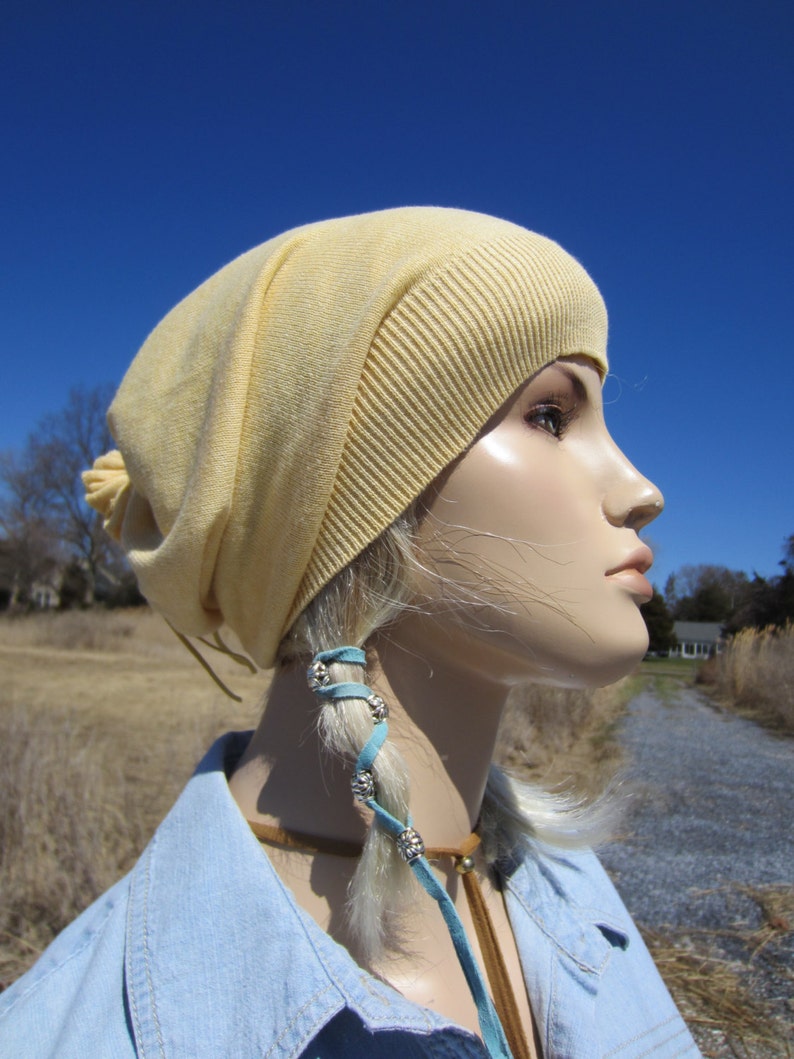 May include: A pale yellow slouchy beanie with a long blue leather cord with silver beads. The beanie is worn by a mannequin with blonde hair.