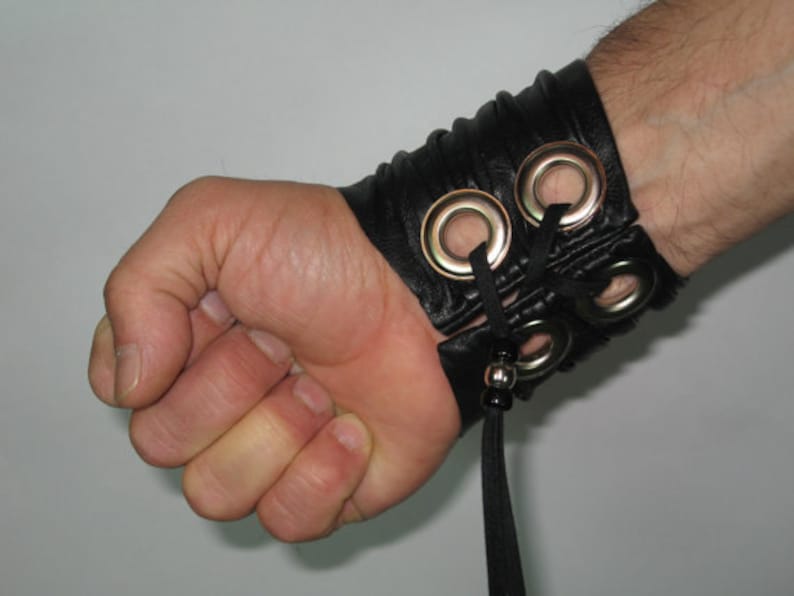 May include: Black leather bracelet with silver eyelets and a black tassel. The bracelet is adjustable and can be worn on the wrist or arm.
