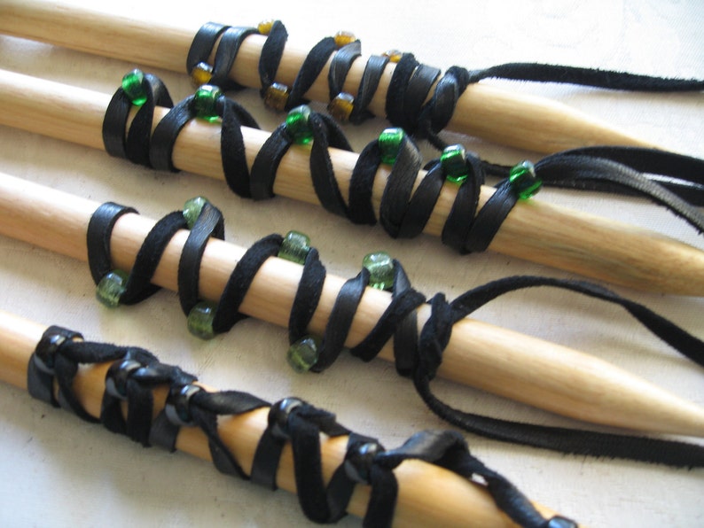 May include: Wooden dowels wrapped with black leather and adorned with green and amber beads. The leather is spiraled around the dowels, creating a decorative pattern. Some dowels have leather tassels.