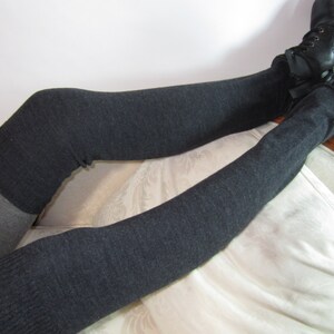 K&ouml;nnte beinhalten: Kniestr&uuml;mpfe in Anthrazitgrau und Hellgrau. Die Socken werden mit schwarzen Schn&uuml;rstiefeln kombiniert. Die Socken sind aus weichem Strickmaterial. Die Person sitzt auf einem wei&szlig; gepolsterten Stuhl.