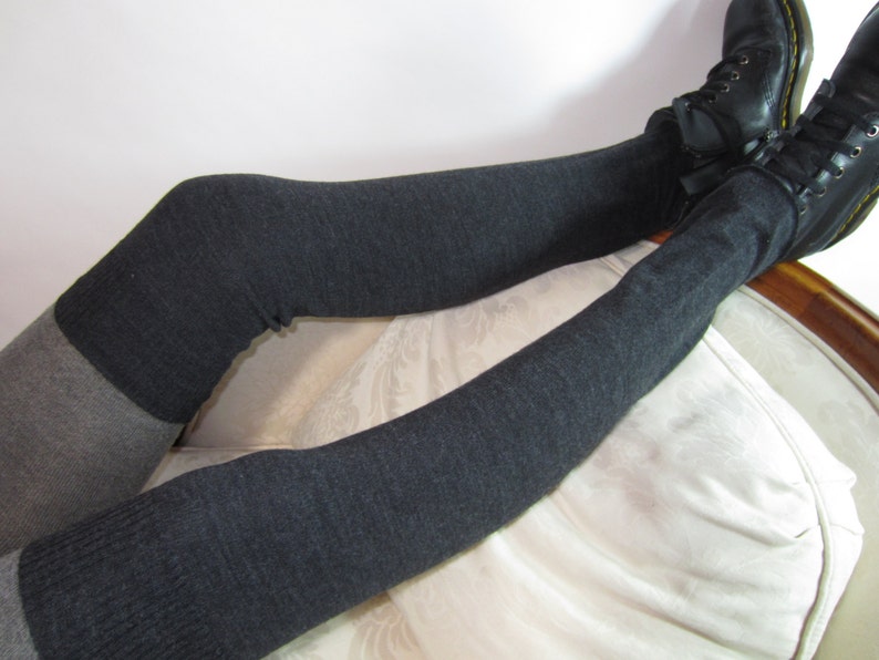 K&ouml;nnte beinhalten: Kniestr&uuml;mpfe in Anthrazitgrau und Hellgrau. Die Socken werden mit schwarzen Schn&uuml;rstiefeln kombiniert. Die Socken sind aus weichem Strickmaterial. Die Person sitzt auf einem wei&szlig; gepolsterten Stuhl.