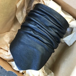 May include: A black leather cuff bracelet with a wrinkled texture. The bracelet is in a brown cardboard box with tissue paper.