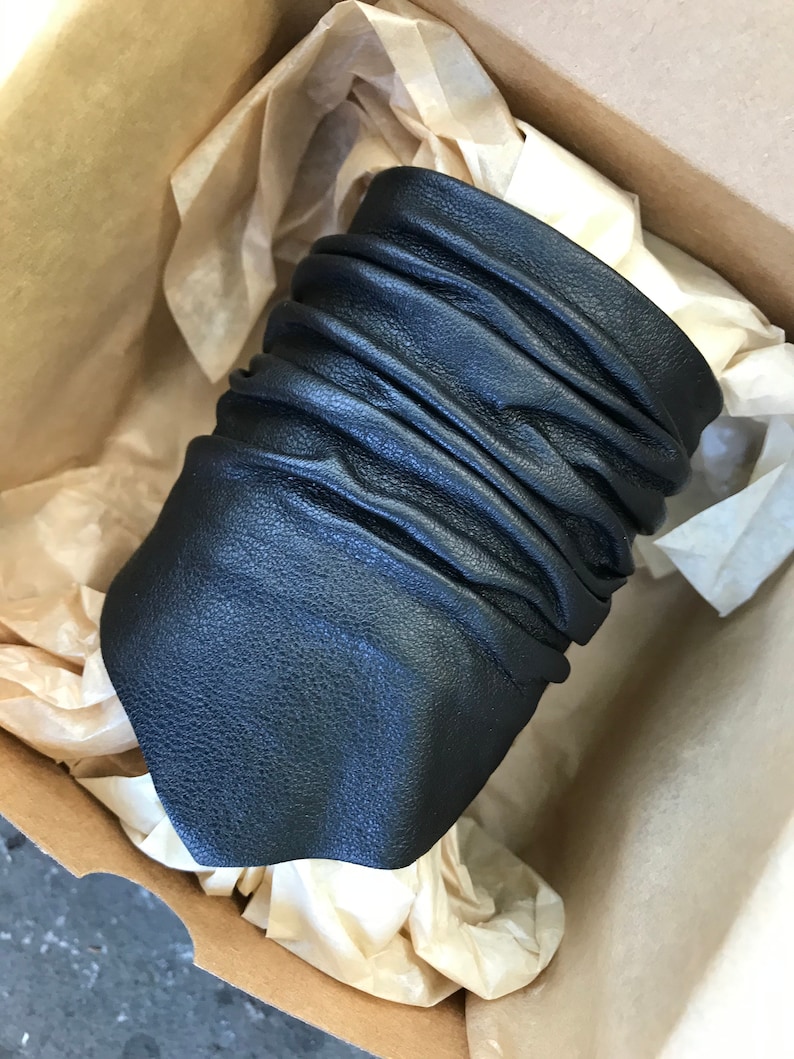 May include: A black leather cuff bracelet with a wrinkled texture. The bracelet is in a brown cardboard box with tissue paper.