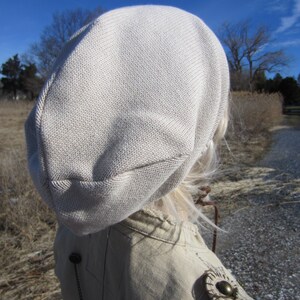 May include: A beige knitted beanie with a slouchy fit. The beanie is made of a soft, comfortable material and has a simple, classic design.