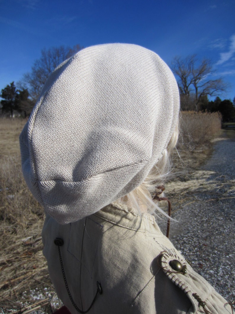 May include: A beige knitted beanie with a slouchy fit. The beanie is made of a soft, comfortable material and has a simple, classic design.