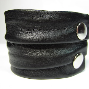 May include: A black leather bracelet with two silver metal snaps.