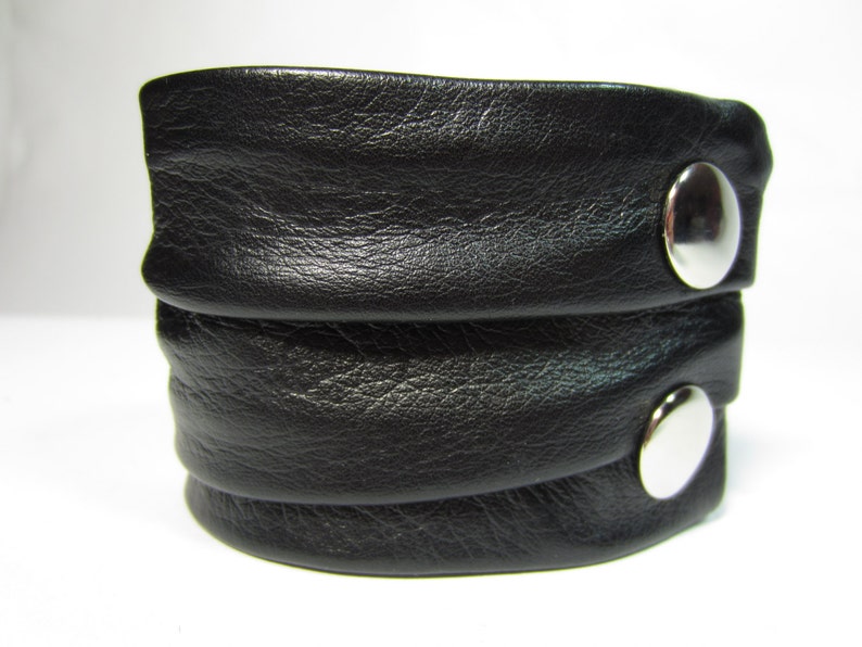 May include: A black leather bracelet with two silver metal snaps.