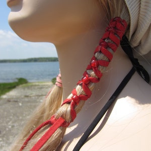 May include: Red leather hair tie with beads woven into the leather. The hair tie is tied around a woman's blonde hair.