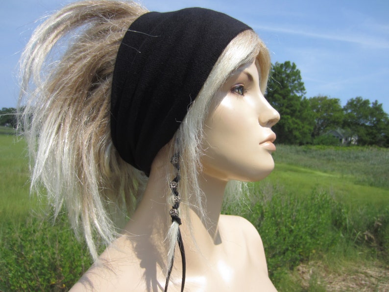 May include: A black headband worn on a mannequin with blonde hair. The headband is made of a soft, stretchy fabric. The mannequin is wearing a beaded hair tie on one side.