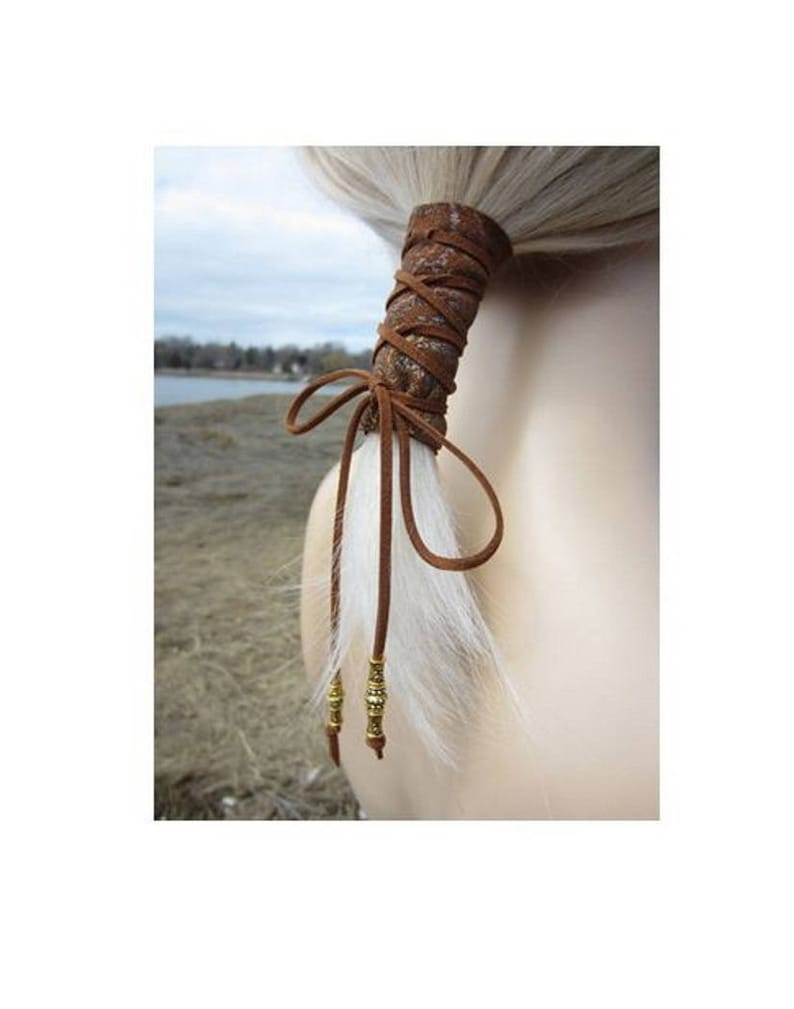 May include: Brown leather ponytail holder with a braided design and gold beads. The holder is tied in a bow and has a white feather accent.