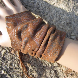 May include: A brown suede wristlet with a silver paisley pattern and a brown leather drawstring closure.