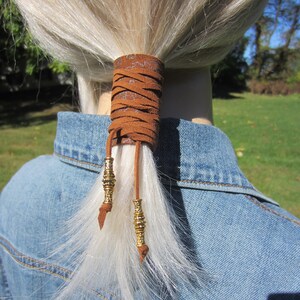 May include: Brown leather ponytail holder with gold beads and a braided design.