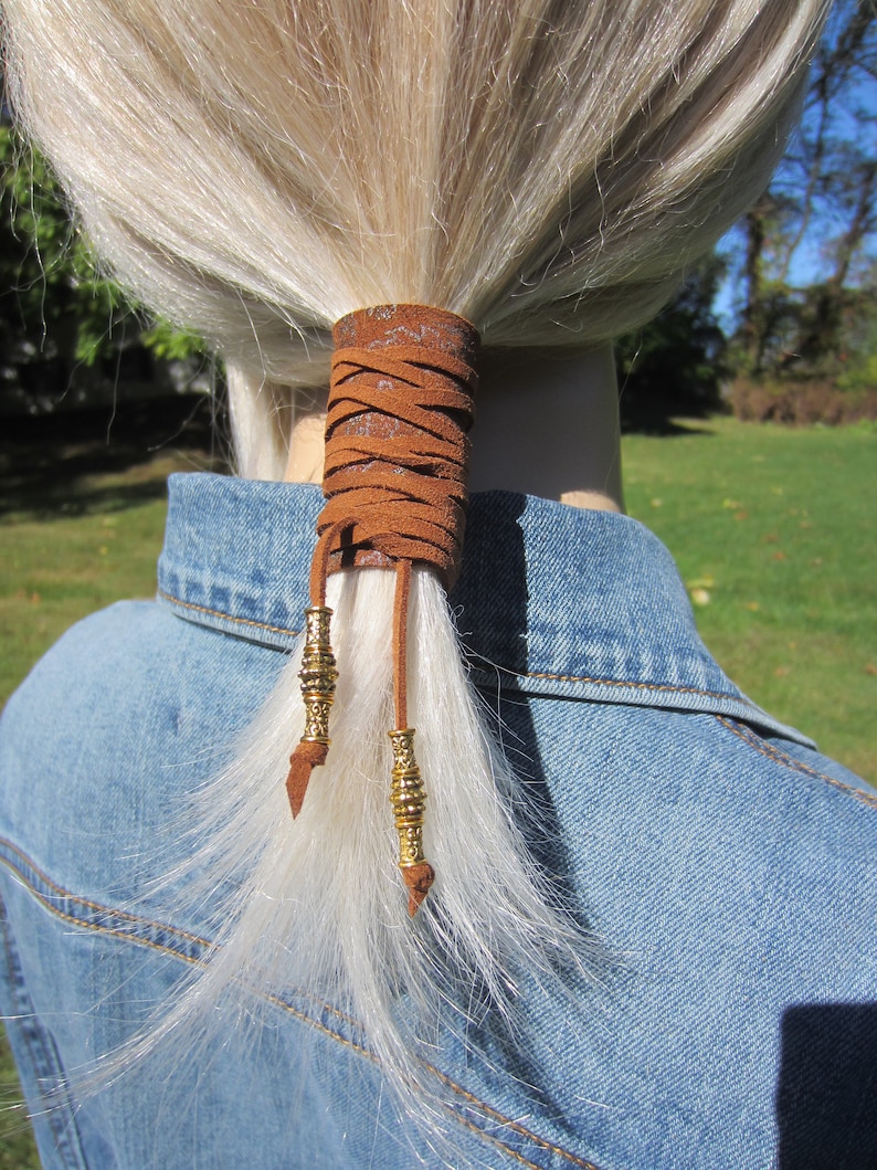 May include: Brown leather ponytail holder with gold beads and a braided design.