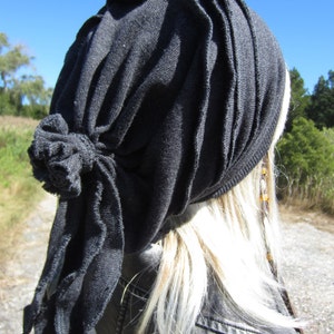 May include: A black fabric head wrap with a knotted detail. The wrap is worn on a person with long, blonde hair.