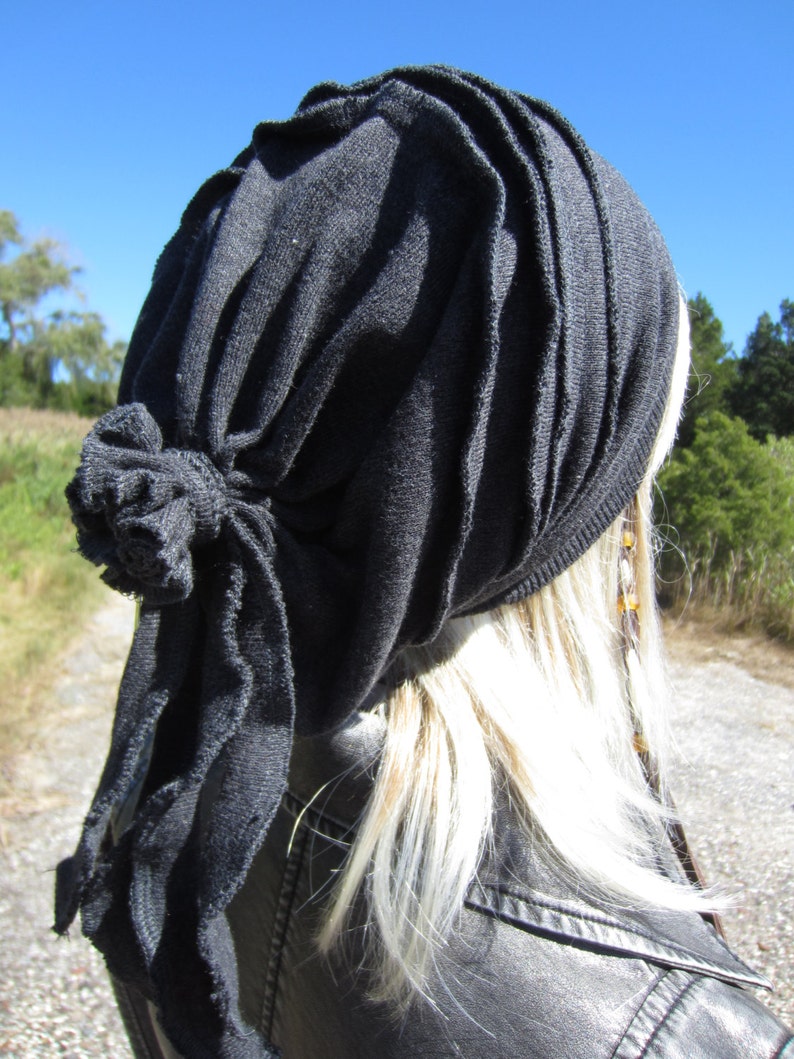 May include: A black fabric head wrap with a knotted detail. The wrap is worn on a person with long, blonde hair.