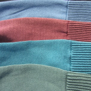 May include: Four knitted fabric swatches in different colors: teal, dark blue, burgundy, and dark gray. The swatches are arranged side by side, with the teal swatch on the left and the dark gray swatch on the right.