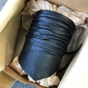 May include: A black leather cuff bracelet with a folded design. The bracelet is in a box with tissue paper.