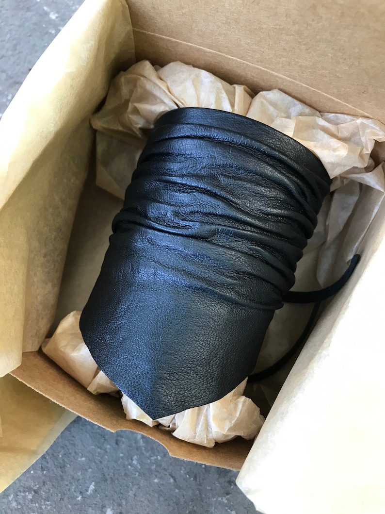 May include: A black leather cuff bracelet with a folded design. The bracelet is in a box with tissue paper.
