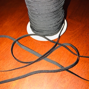 May include: A spool of black elastic cord, wound tightly and ready to be used for sewing or crafting projects.