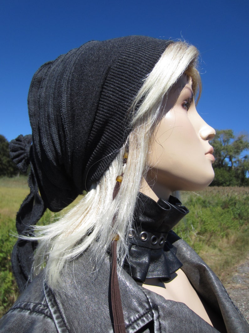 May include: A woman with blonde hair is wearing a black knit beanie with a long brown tassel. She is also wearing a black leather choker with silver grommets and a black leather jacket.