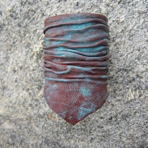 May include: A brown leather cuff bracelet with a turquoise patina. The bracelet is made of several layers of leather that have been folded and stitched together.