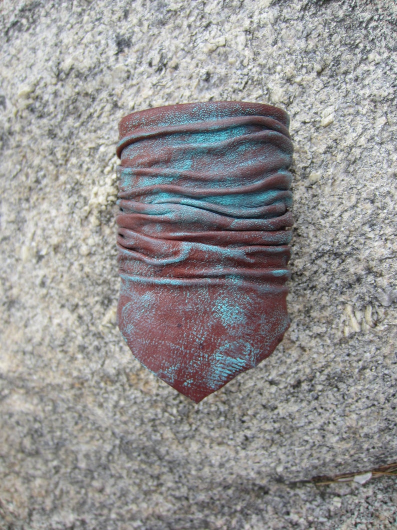 May include: A brown leather cuff bracelet with a turquoise patina. The bracelet is made of several layers of leather that have been folded and stitched together.
