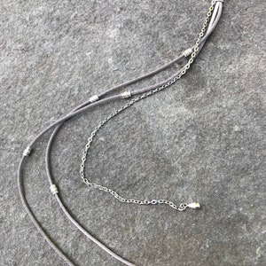 May include: A gray hair clip with three strands of gray cord and a silver chain. The cord has silver beads and the chain has a silver clasp.