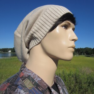 May include: A beige slouchy beanie with a ribbed texture. The beanie is worn by a person with black hair.
