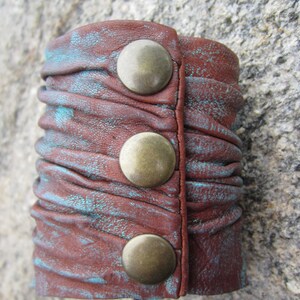 May include: A brown leather cuff bracelet with turquoise accents and three brass-colored metal snaps.