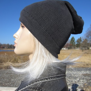 May include: A black beanie with a slouchy fit. The beanie is made of a soft, knitted fabric. The beanie is worn by a person with long, white hair.