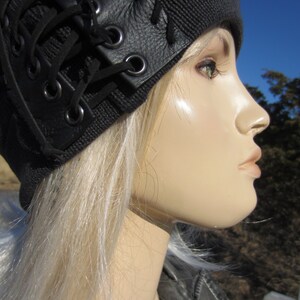 May include: A black beanie with a leather lace-up detail. The beanie is worn by a mannequin with blonde hair.
