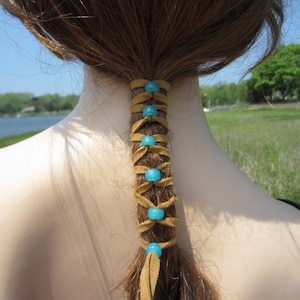 May include: A brown leather hair tie with turquoise beads woven into the design. The hair tie is tied around a ponytail.