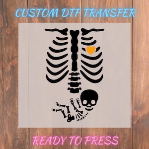 May include: A black skeleton design with a yellow heart and a baby skeleton, printed on a light background. The text "CUSTOM DTF TRANSFER" is at the top, and "READY TO PRESS" is at the bottom.