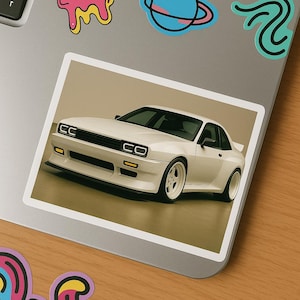 Könnte beinhalten: Weißer Sportwagen-Aufkleber mit schwarzen Akzenten. Das Auto hat ein schlankes Design mit niedrigem Profil, mit Frontspoiler und Spezialrädern. Der Aufkleber befindet sich auf einem Laptop.