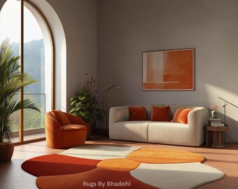 May include: A modern living room featuring a cream-colored sofa with orange pillows, an orange armchair, and a unique flower-shaped rug in shades of orange, white, and red. The room has a large arched window and a painting on the wall. The text "Rugs By Bhadohi" is visible.