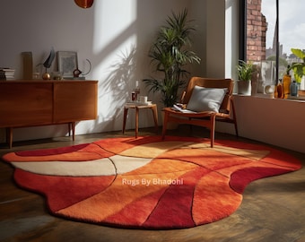 May include: A vibrant, abstract area rug in shades of red, orange, and cream. The rug features a unique, flowing design with curved lines and varying textures. The rug is placed on a dark wood floor in a well-lit room.