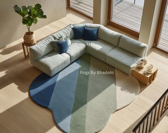 Puede incluir: Vista aérea de un salón moderno con un gran sofá esquinero verde claro y cojines azules. Una alfombra colorida en forma de nube en tonos azules, verdes y blancos está sobre el suelo de madera. También se ve una pequeña mesa auxiliar y una planta en maceta.