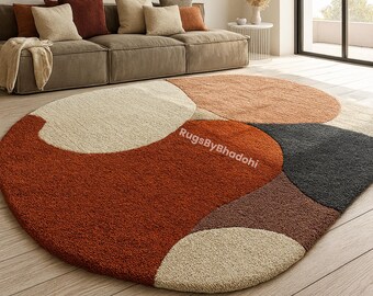May include: A round, abstract area rug with a geometric design. The rug features a combination of colors, including rust, beige, brown, and gray. The rug is placed on a hardwood floor, with a sofa and pillows in the background.
