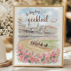 Puede incluir: Una impresión en acuarela enmarcada con un borde dorado. La obra de arte representa una carrera de caballos en un hipódromo, con las palabras "Derby Day Cocktail Bar" en una escritura elegante. Flores rosas y rojas enmarcan la parte inferior de la imagen.