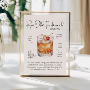 May include: A framed sign featuring a Rum Old Fashioned cocktail recipe. The graphic displays a crystal glass with amber liquid, a large ice cube, an orange peel, and a cherry. Text lists ingredients including 2 oz aged rum, 1/4 oz simple syrup, and 2-3 dashes Angostura bitters.