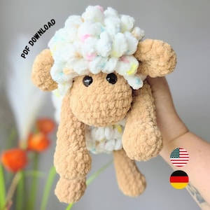 Könnte beinhalten: Ein gehäkeltes Schaf-Stofftier mit beigefarbenem Körper und einem flauschigen weißen Kopf mit bunten Pastellsprenkeln. Das Spielzeug hat zwei schwarze Kunststoffaugen und lange, herabhängende Gliedmaßen. Der Text PDF DOWNLOAD ist oben links sichtbar.