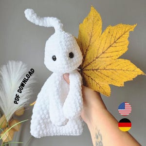 May include: A white crocheted ghost plush toy with a small antenna-like protrusion on its head and two black bead eyes. The ghost is held next to a large, yellow, dried maple leaf. The image includes the text PDF DOWNLOAD.