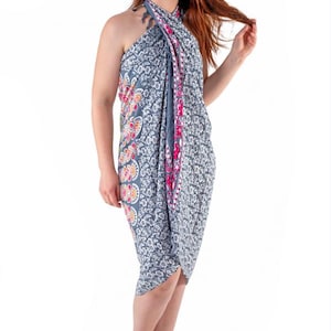 Może przedstawiać: Szary i biały wzorzysty sarong z kwiatowym wzorem i różowymi akcentami. Sarong jest owinięty wokół ciała i zawiązany na szyi. Modelka stoi boso.