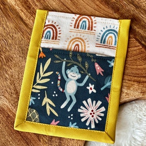 May include: A yellow fabric pouch with a blue and white fabric lining. The lining features a pattern of rainbows and the pouch features a pattern of monkeys, flowers, and leaves.