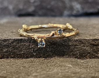 May include: A gold ring with a twig design and three small blue gemstones.