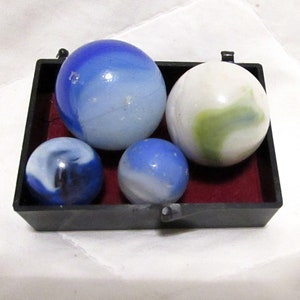 May include: Four glass marbles in a black tray. The marbles are white with blue, green, and black swirls.