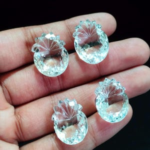 以下が含まれることがあります： パイナップルの形をした4つの透明で無色のファセットカットされた宝石。各石は、三角形のファセットを持つ丸みを帯びたベースと、パイナップルの葉を模した放射状の線が刻まれた上部セクションで構成されています。